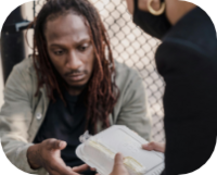 homeless man receiving meal from a woman in a mask