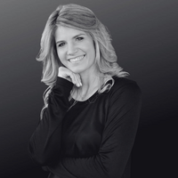 Jessica wearing a white blazer, smiling as she writes in her planner