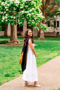 Law school graduate wearing hood with her white grad dress near a flowering tree