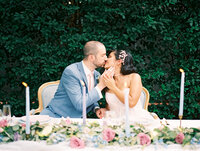 bride and groom kissing while sitting at their sweetheart table in the garden patio of a historic old town alexandria home venue