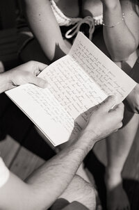Black and white film photo of a groom reading a handwritten letter before the wedding ceremony — a quiet, intimate moment captured by a film wedding photographer.