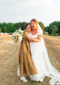 Bailee in a yellow dress hugging one of her brides
