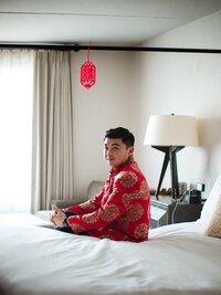 portrait of Chinese groom sitting on side of bed