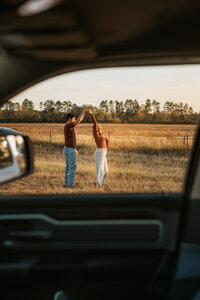Couple dancing together in an open farm field in Aiken, SC photographed through a truck window during a sunset couples session.