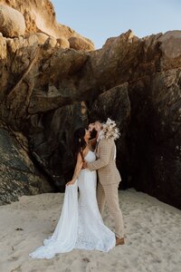 bride and groom embracing on a beach in front of rocks