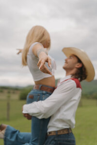 A young man in a cowboy hat picks up his girlfriend while she holds out her arms as he spins her in Northeast, TN