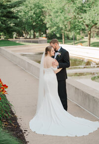 A bride and groom stand near a fountain by the Ford Museum in Grand Rapids