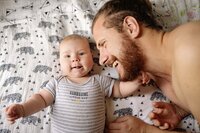 Père qui rigole avec son bébé sur un lit