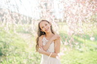 A young girl in a white dress stands under a blooming tree smiling