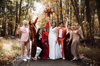 A bride lifts her bouquest and celebrates joyously with her bridal party at her family farm