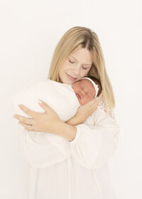 Mama snuggling her newborn baby girl in white wrap