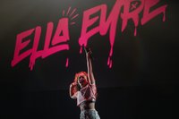 Photograph of ella Eyre stood under neon pink sign of her name raising hand to crowd
