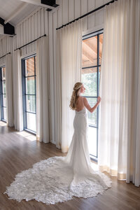 bride in wedding gown looking through curtains at Milestone Georgetown Texas by Firefly Photography