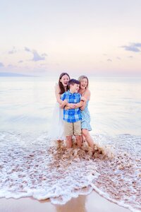 Pregnant woman sitting on the sand in Wailea getting splashed by wave during her maternity portraits