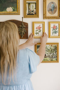 Woman in a light blue dress arranging framed florals on the wall