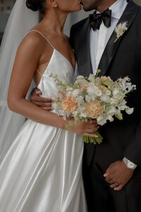 elegant bride holding bouquet and groom kissing