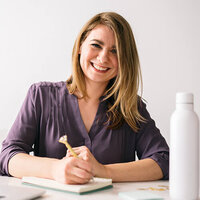 Darcie Milfeld in a purple shirt sitting at a desk writing on a notepad