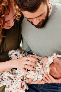 New parents holding and looking at their swaddled baby.  Mom has her hand resting on baby's belly.  Photo taken by Philadelphia maternity photographer, Kristi