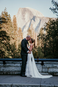Bride and groom embracing in front of Half Dome at Glacier Point during their Yosemite National Park elopement, surrounded by pine trees and golden hour light.