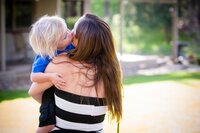 Woman holding her toddler as he kisses her on the cheek