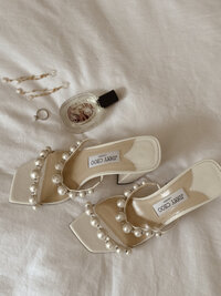 Flat lay of pearl-embellished Jimmy Choo heels with perfume and jewelry on linen