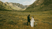 bride and groom holding hands by a lake in colorado