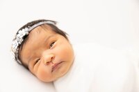 two week old baby boy sleeping posed with a blue knitted blanket over back.