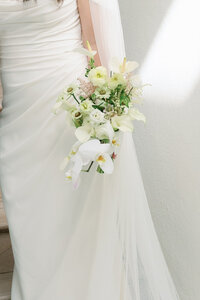 Close up of bride holding white bouquet beside her dress
