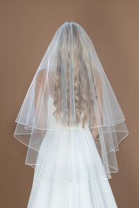 Bride wearing a fingertip length circle veil with blusher and small ribbon edge, and holding a white and blush bouquet