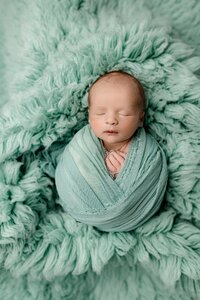 little infant baby boy wrapped in sea green on a matching fur rug
