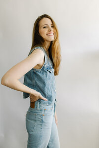 A woman smiles at the camera with her hand on her hip against a white background in a personal brand photo.