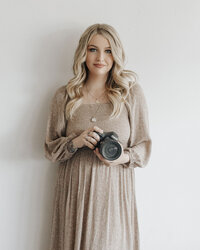 Haley McElroy wearing tan floral dress and holding a camera while looking forward