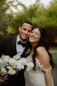 A couple in wedding attire smiles at the camera.