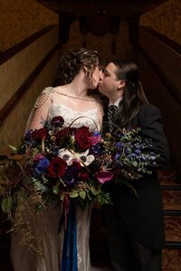 Bride and groom kissing on staircase with large floral bouquet