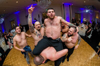 Man being hoisted up shirtless on the dance floor, capturing the raw energy of photojournalistic wedding photography.