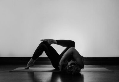 fallback shared on Invalid Date | Black and white image of Alex Paige on a yoga mat in a variation of a figure four pose w...