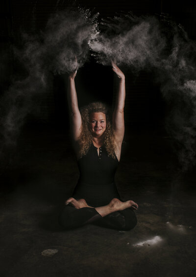 fallback shared on Invalid Date | Alex Paige sitting in lotus pose wearing all black throwing powder overhead
