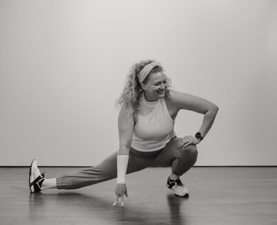 fallback shared on Invalid Date | Alex Paige doing a deep side lunge smiling and looking to the side in a black and white 