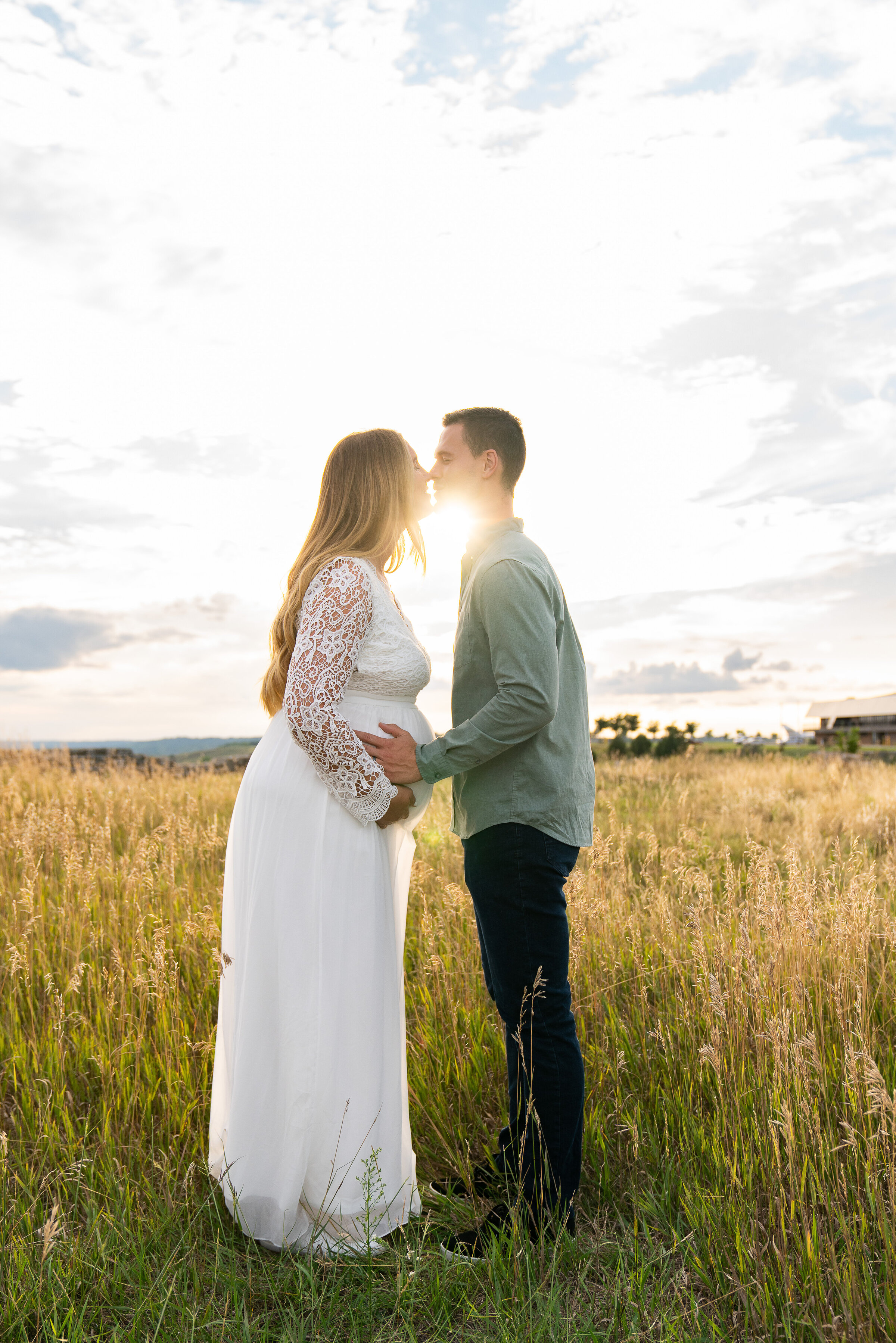Couple kissing during their maternity photo shoot with the sun peaking behind them.