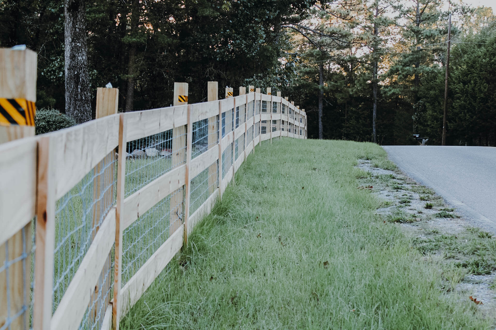 wooden-and-wire-fence-lining-edge-of-grassy-property-next-to-road