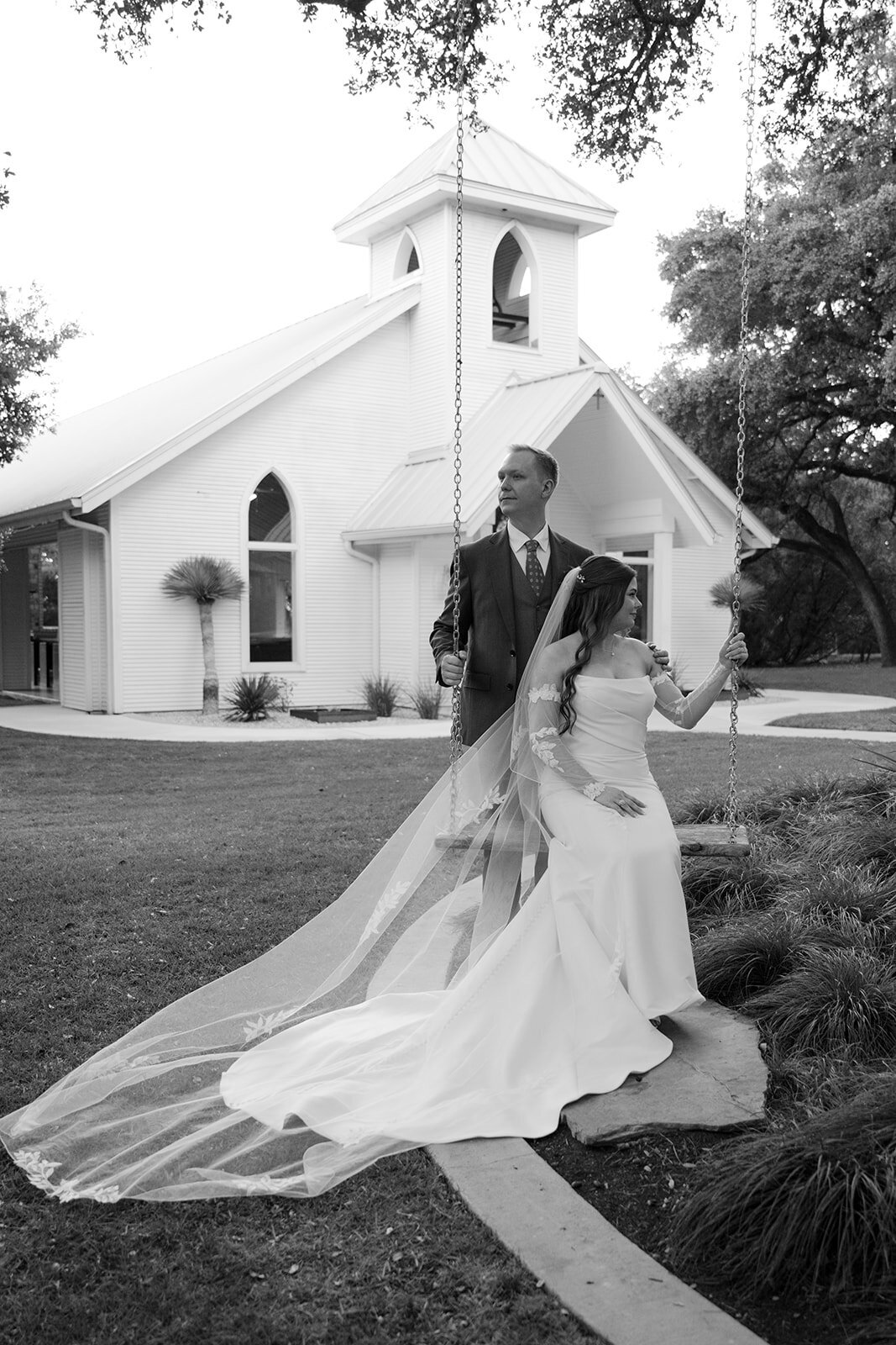 Bride and groom sharing a quiet moment in front of a white chapel at The Gruene Chandelier, captured in black and white for a timeless editorial look.