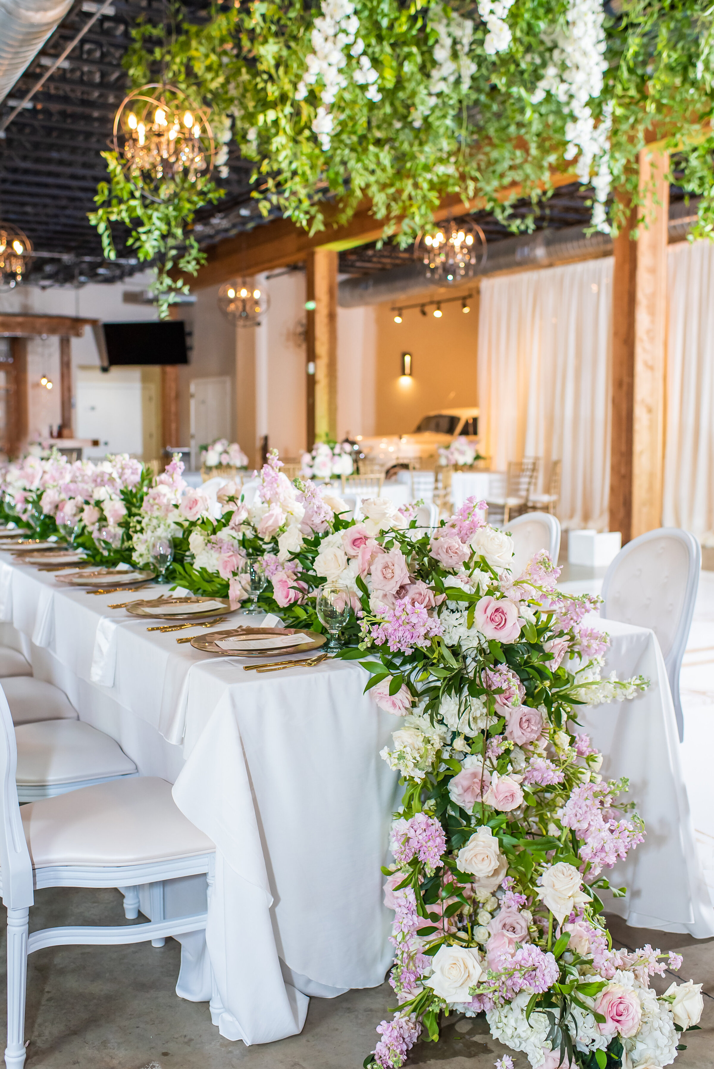 Elegant floral tablescape with cascading blush and ivory blooms, gold flatware, and white linen at a luxury Birmingham wedding reception designed by Wells Design Co.