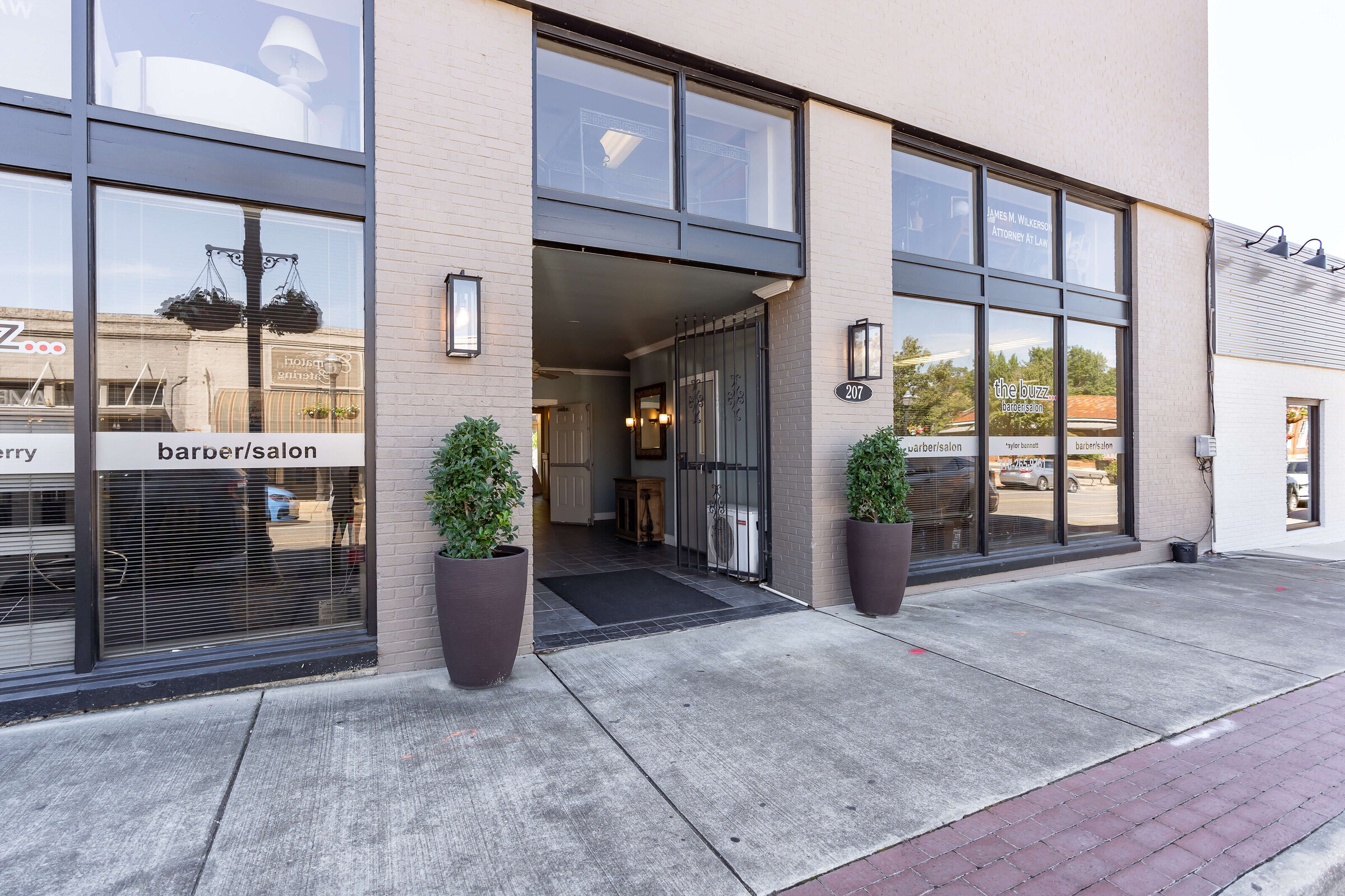 Street-level entrance to a building with large windows, two potted plants by the open doorway.