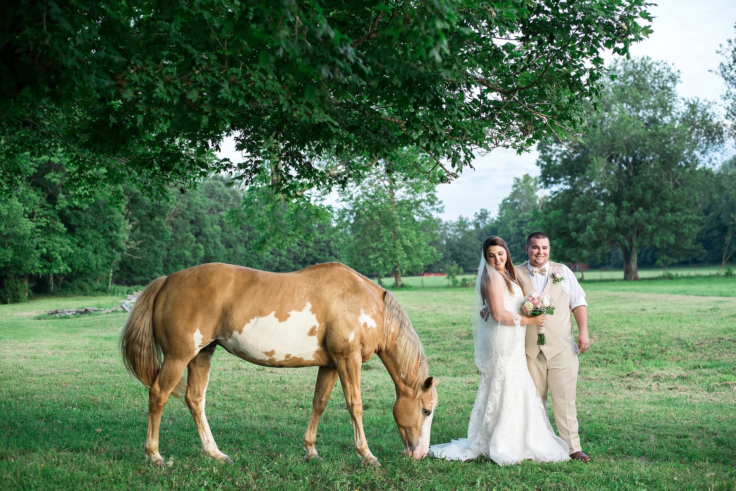 Couple standing together in an open field beside a horse at Cactus Creek Barn