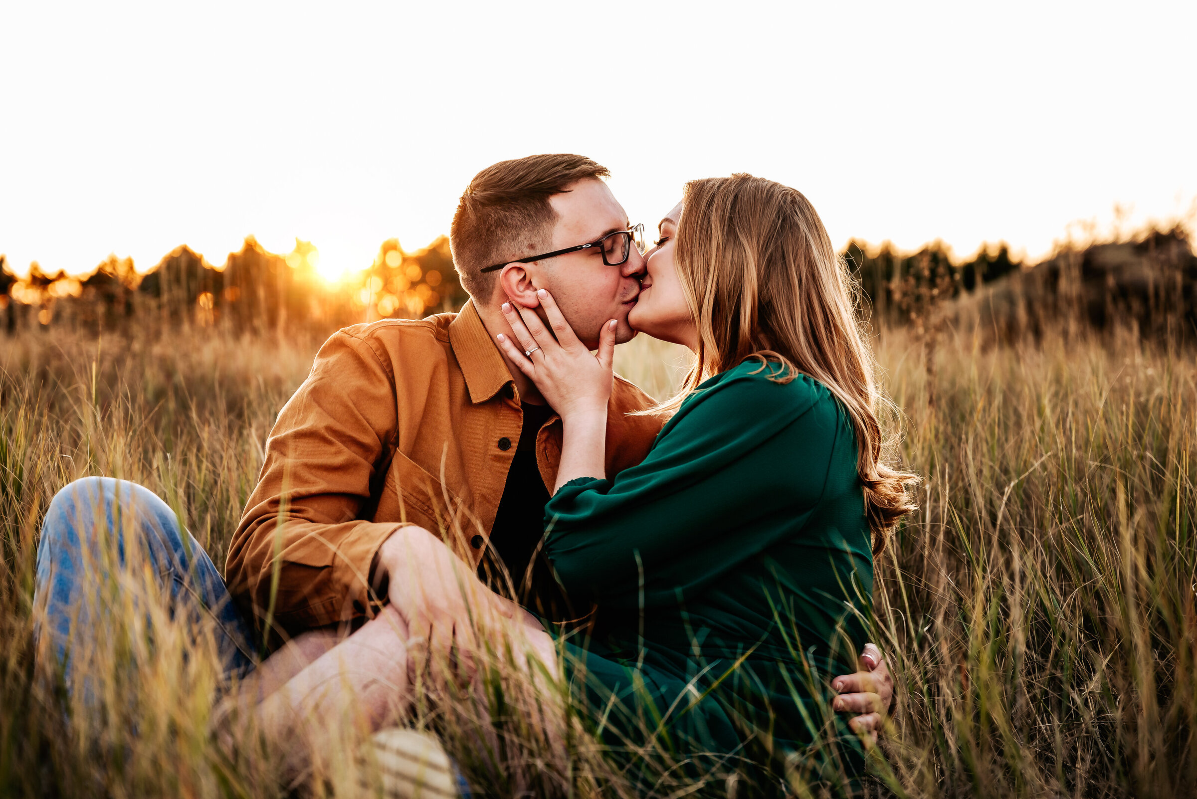 Couple sits in field of long grass and kisses each other