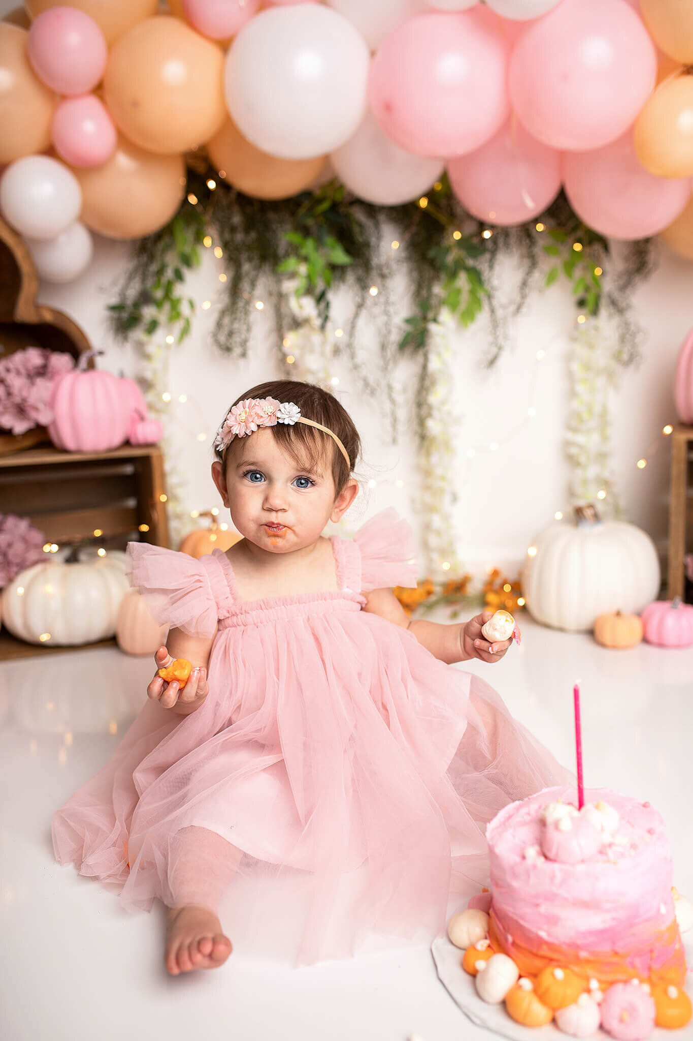 Little 1 year old girl eating small pumpkin cake at cake smash