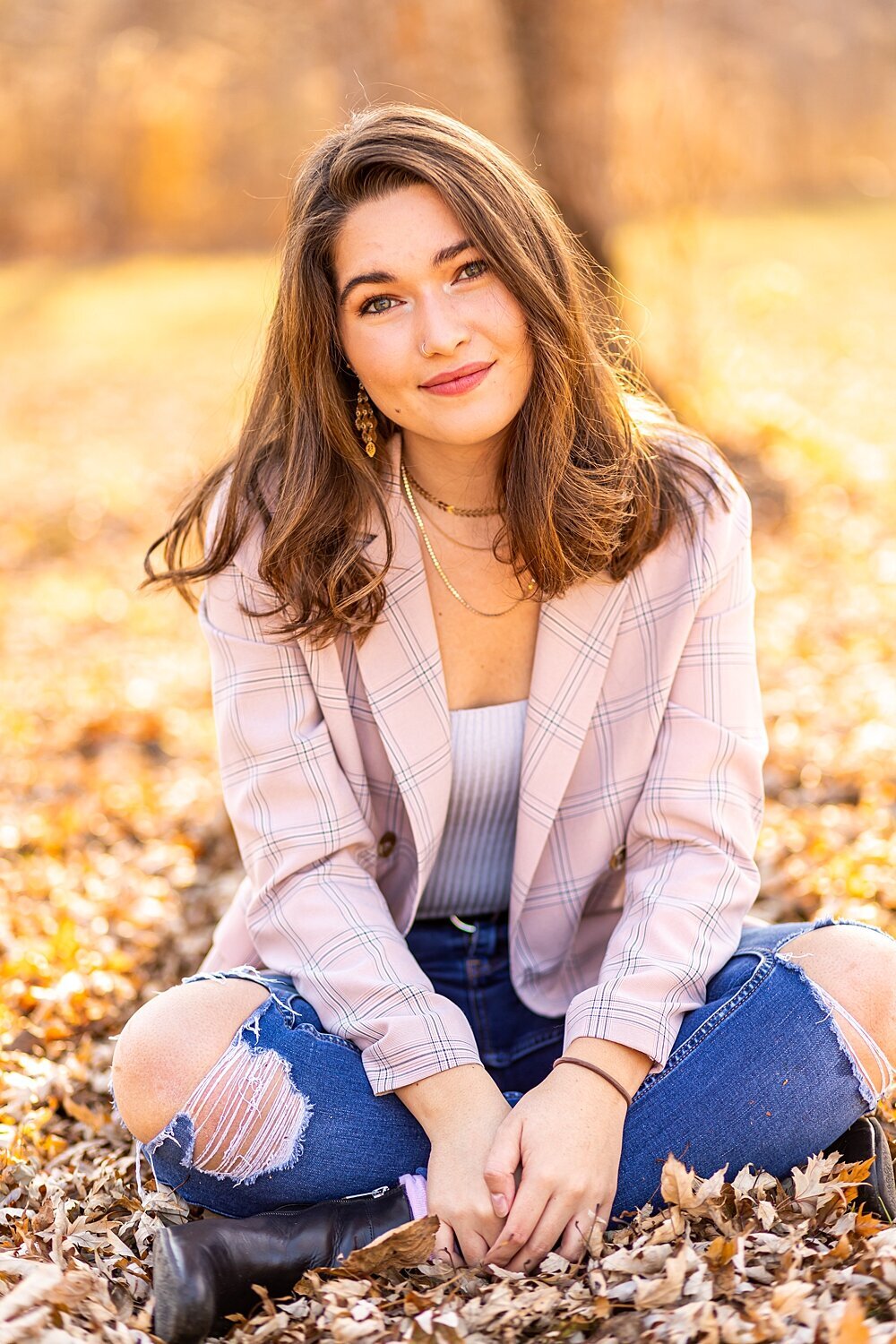 Nh senior girl sits in fall leaves and smiles during fall senior session in Bedford, New Hampshire