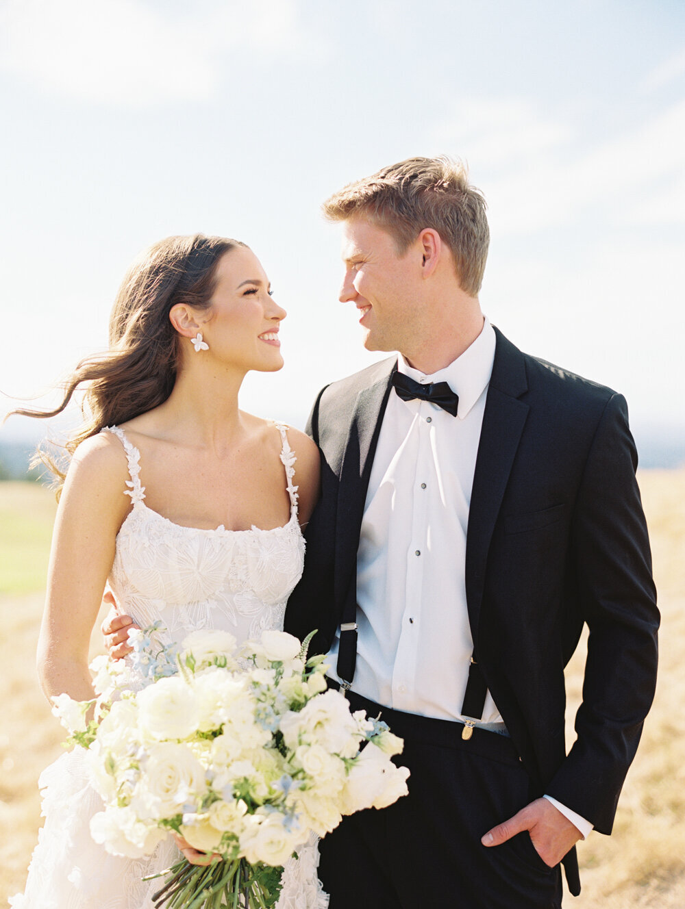 bride looking at groom while holding white rose bouquet hair blowing in wind