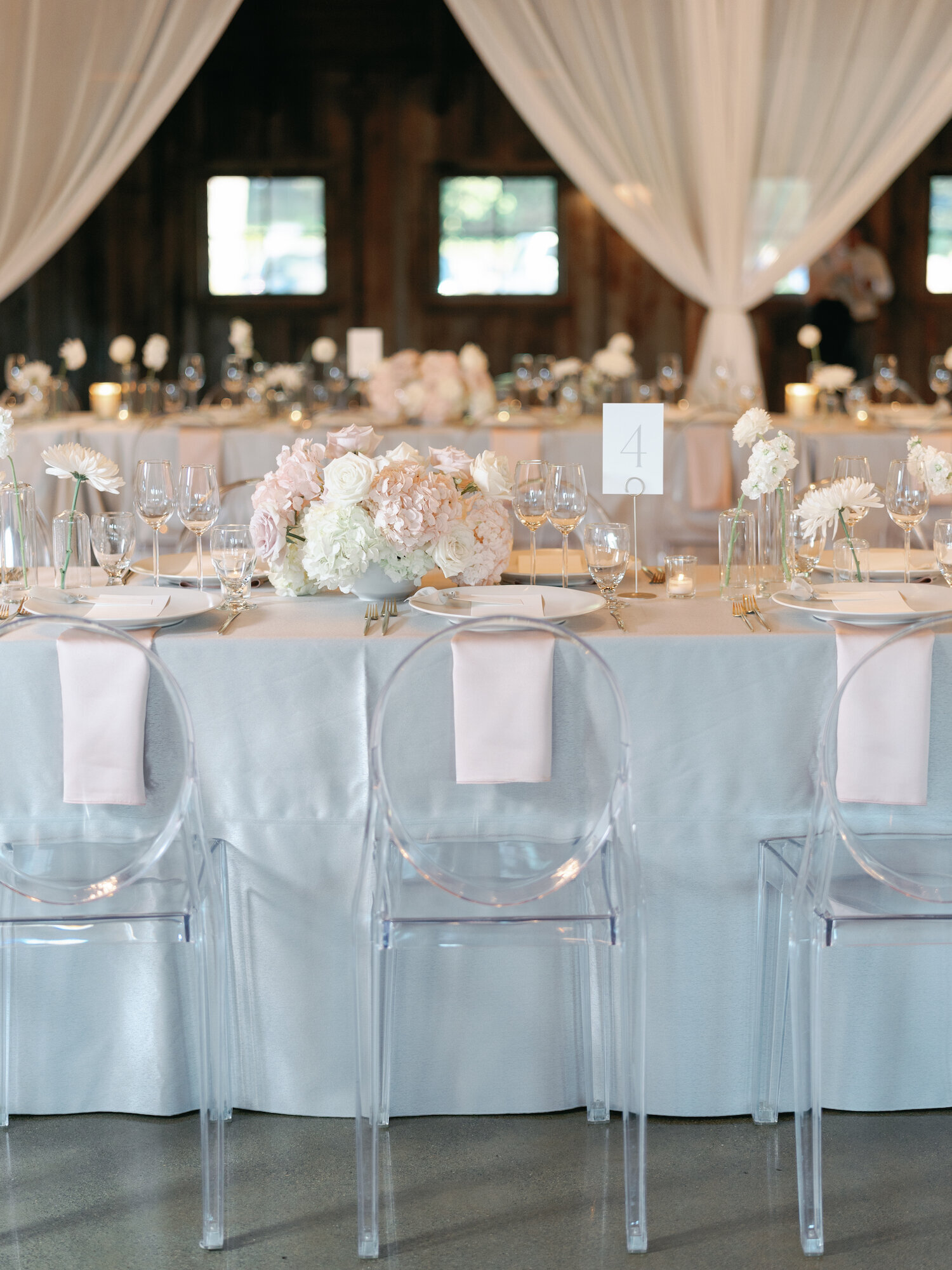 minimalist floral table-scape at wedding reception with ghost chairs in barn