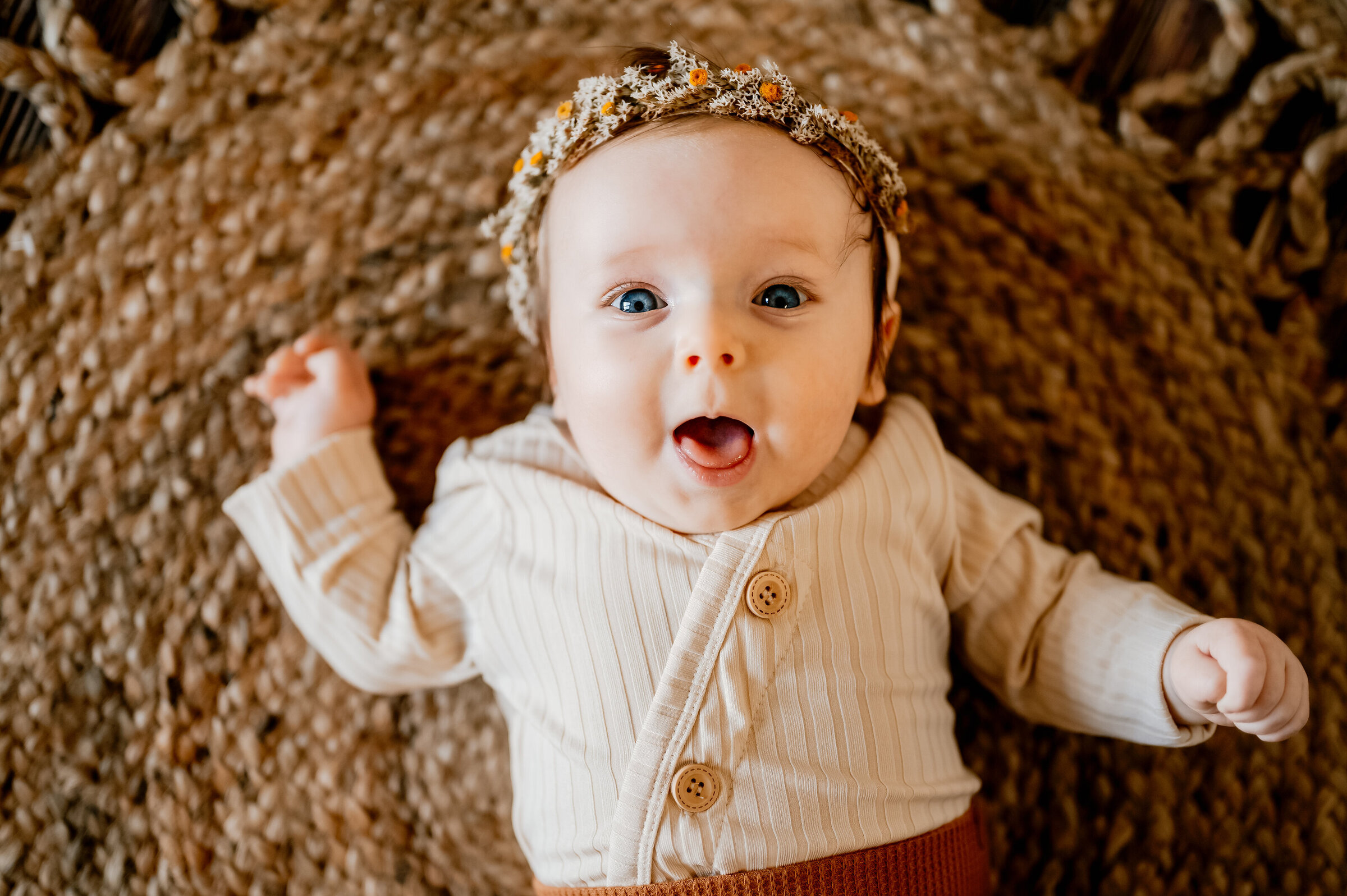baby lays on boho rug and laughs at camera in dried floral headband